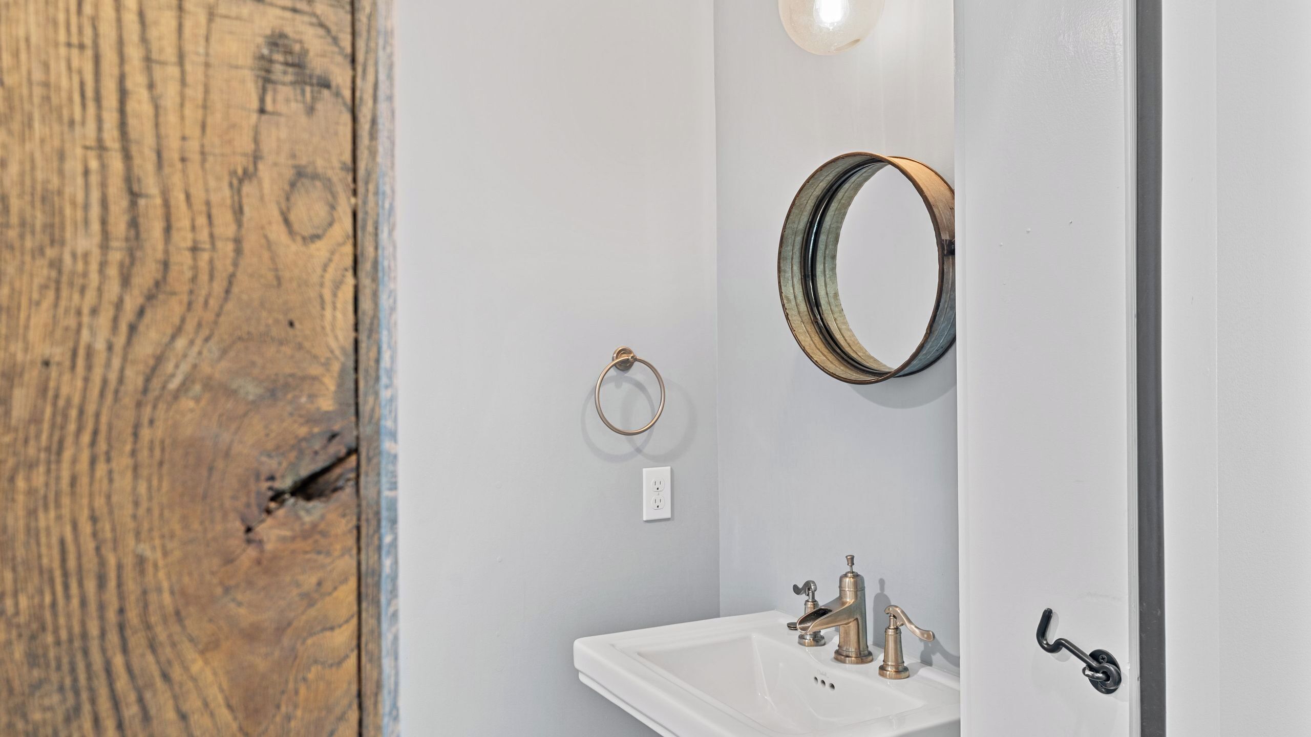 A bathroom with a wooden door, a white sink, and a mirror.