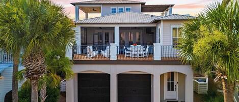 A two-story house with a balcony, garage doors, and palm trees.