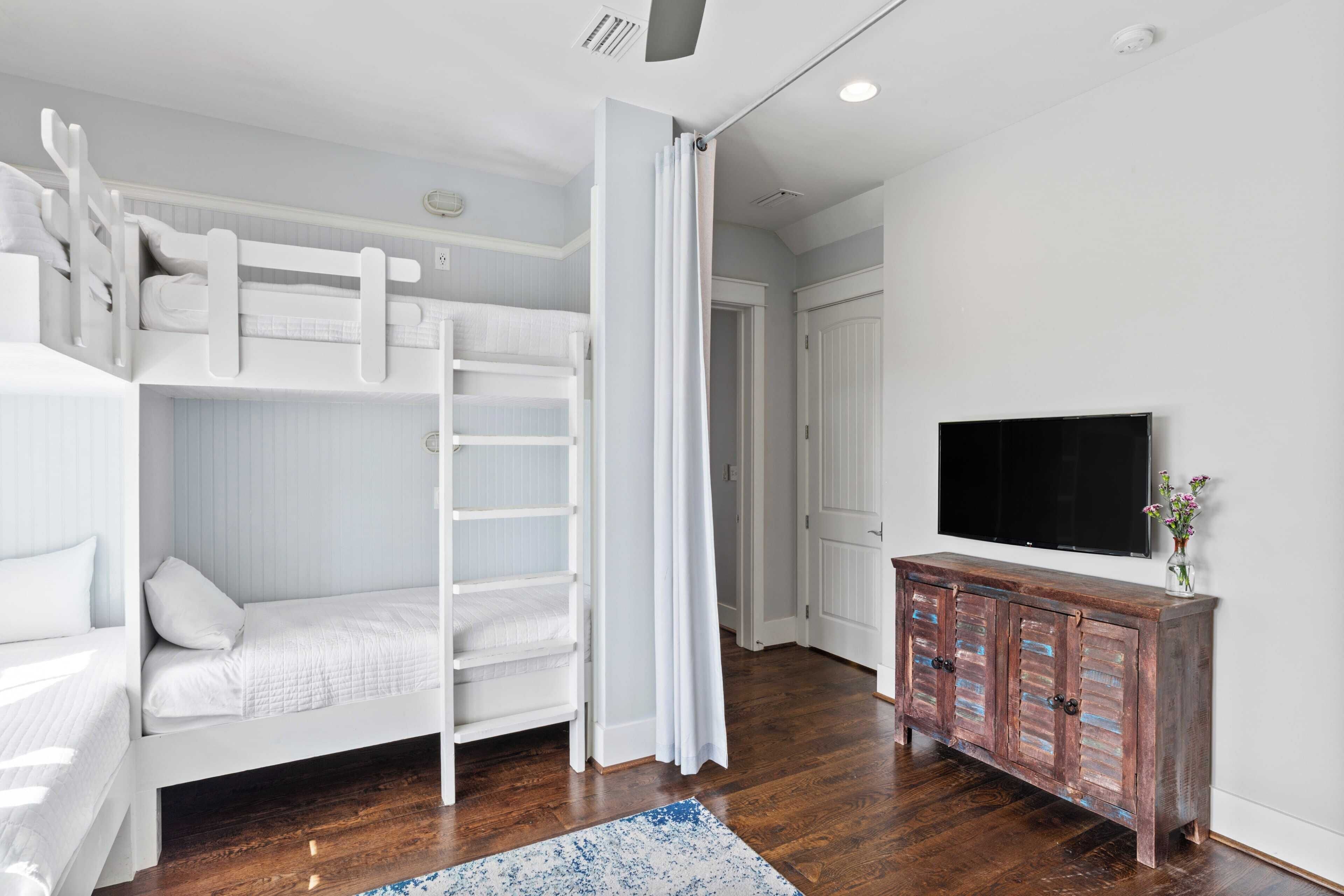 Une pièce avec des lits superposés, une armoire en bois, un téléviseur à écran plat et une porte.