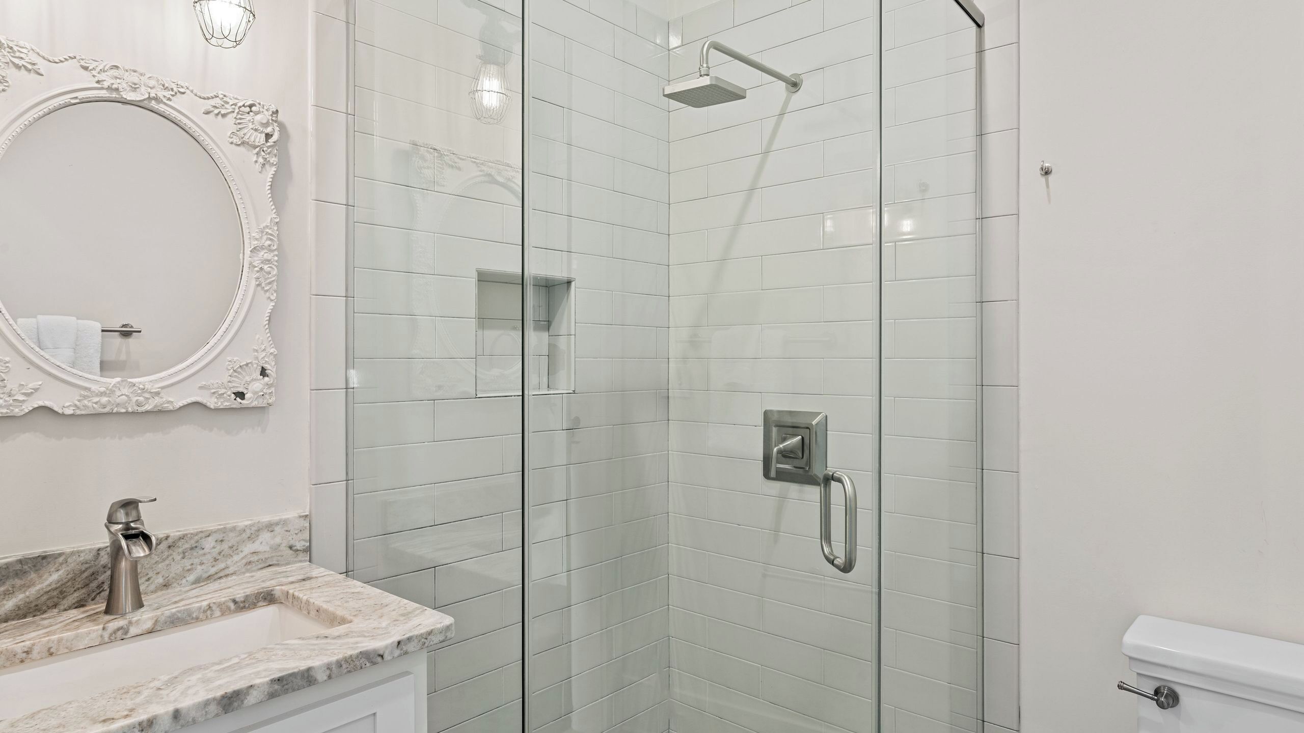 Een badkamer met een douche met glazen wand, een marmeren wastafel, toilet en een spiegel bevestigd aan de muur.