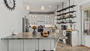 A modern kitchen with white cabinetry, a marble island, pendant lighting, and a built-in oven. - Totally Beachin by Avantstay Sleeps 18 Seacrest Beach (Panama City Beach)