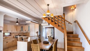 Une cuisine spacieuse avec des meubles en bois et un îlot central, un coin repas avec des chaises en osier et un escalier en bois.