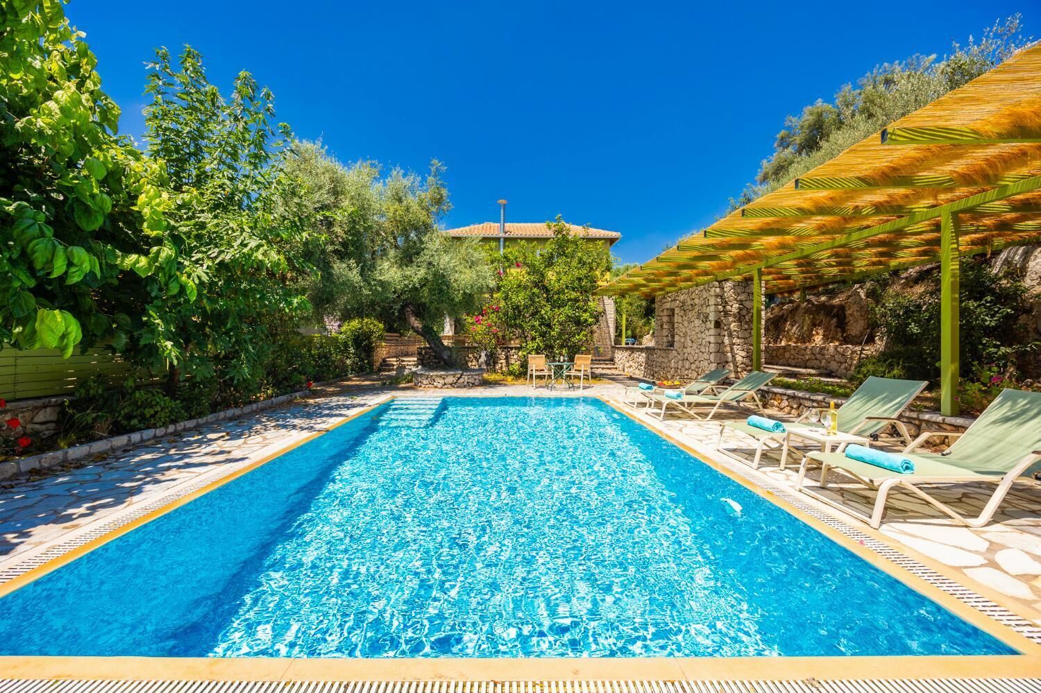 Une piscine rectangulaire à l’eau d’un bleu cristallin, entourée de chaises longues et d’un mur en pierre.