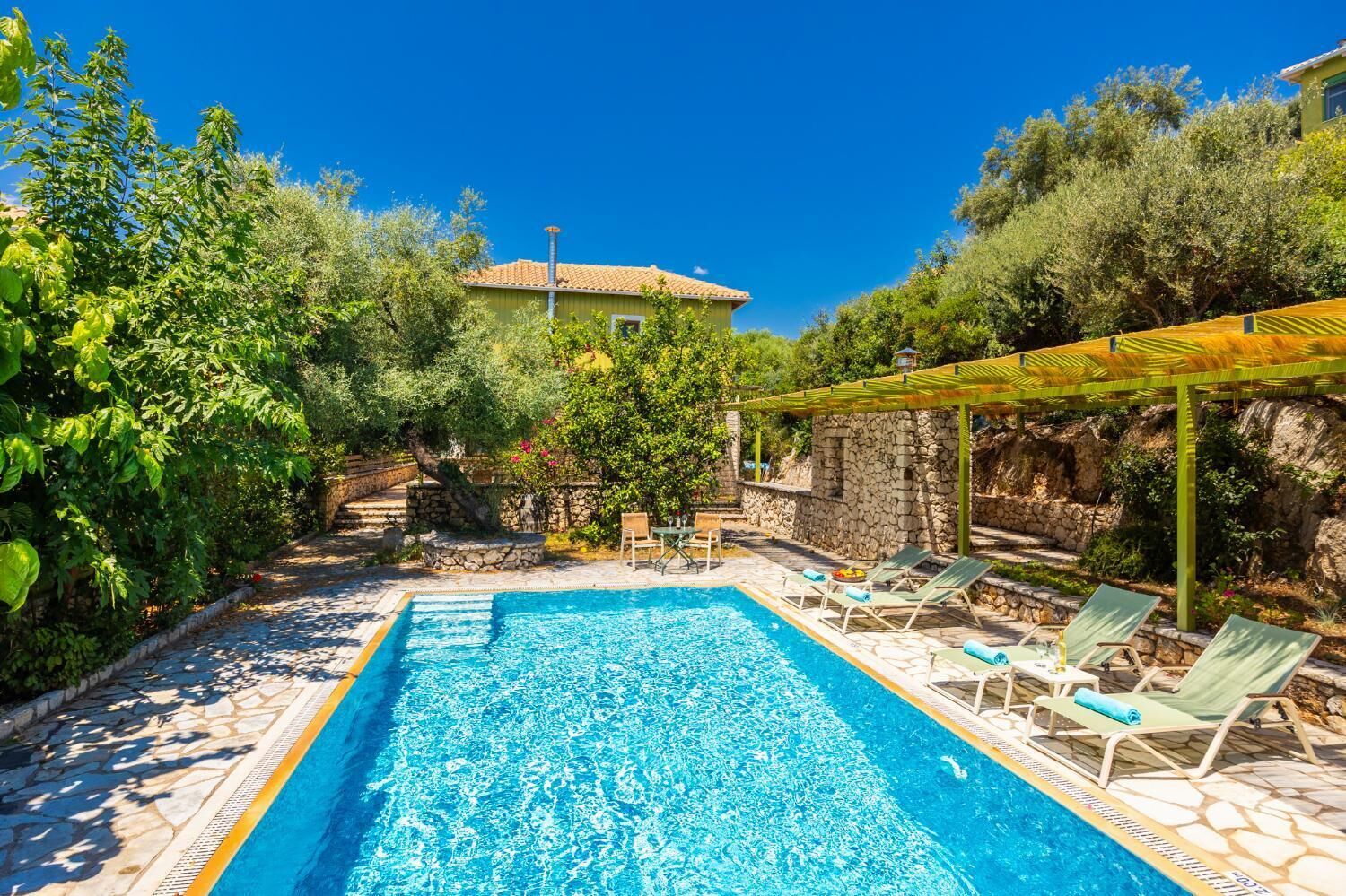 A swimming pool with lounge chairs, surrounded by greenery and stone walls.