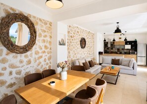 Un espace de vie moderne avec un mur en pierre, un miroir rond, un coin repas doté d’une table en bois et une cuisine équipée d’un four encastré.