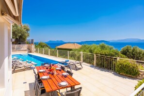 A poolside dining area with a table set for two, a pool, and a view of the sea and mountains. - Villa Cohili - Three Bedroom Villa, Sleeps 6 (Lefkada)