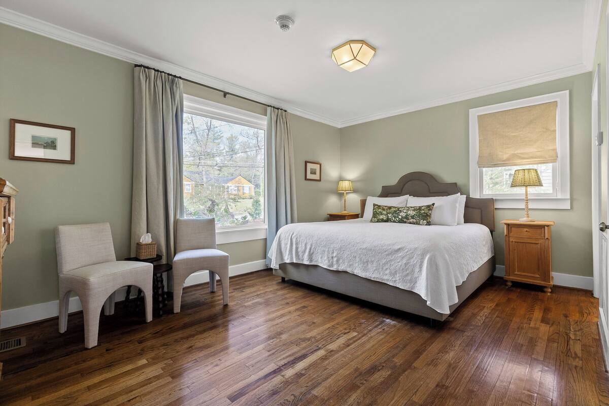 A bedroom with a bed, a chair, a nightstand, a lamp, and a window with curtains.