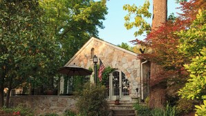 A stone building with a flag, surrounded by lush greenery and a tree with red leaves. - Chanticleer Inn Bed & Breakfast (Lookout Mountain)