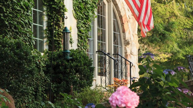 A stone building with ivy, an American flag, and pink hydrangeas in the foreground. - Chanticleer Inn Bed & Breakfast (Lookout Mountain)