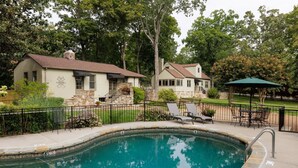 A swimming pool with a stone border, surrounded by a fence, and adjacent to a building with a stone facade and a chimney. - Chanticleer Inn Bed & Breakfast (Lookout Mountain)