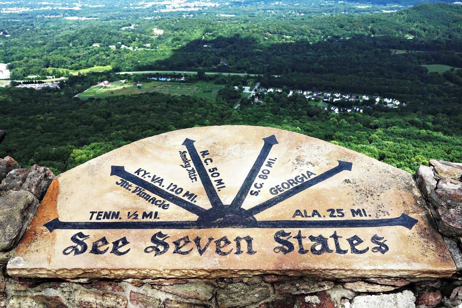 A stone sign with directional arrows pointing to various states and distances.