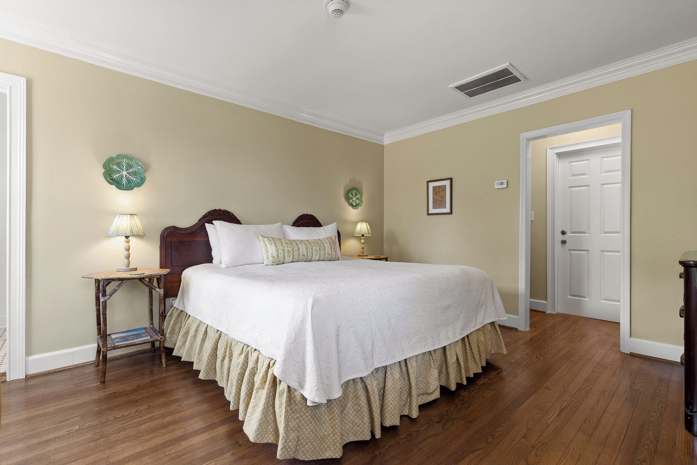 Une chambre à coucher avec un grand lit, deux tables de chevet avec des lampes, une porte et une horloge murale.