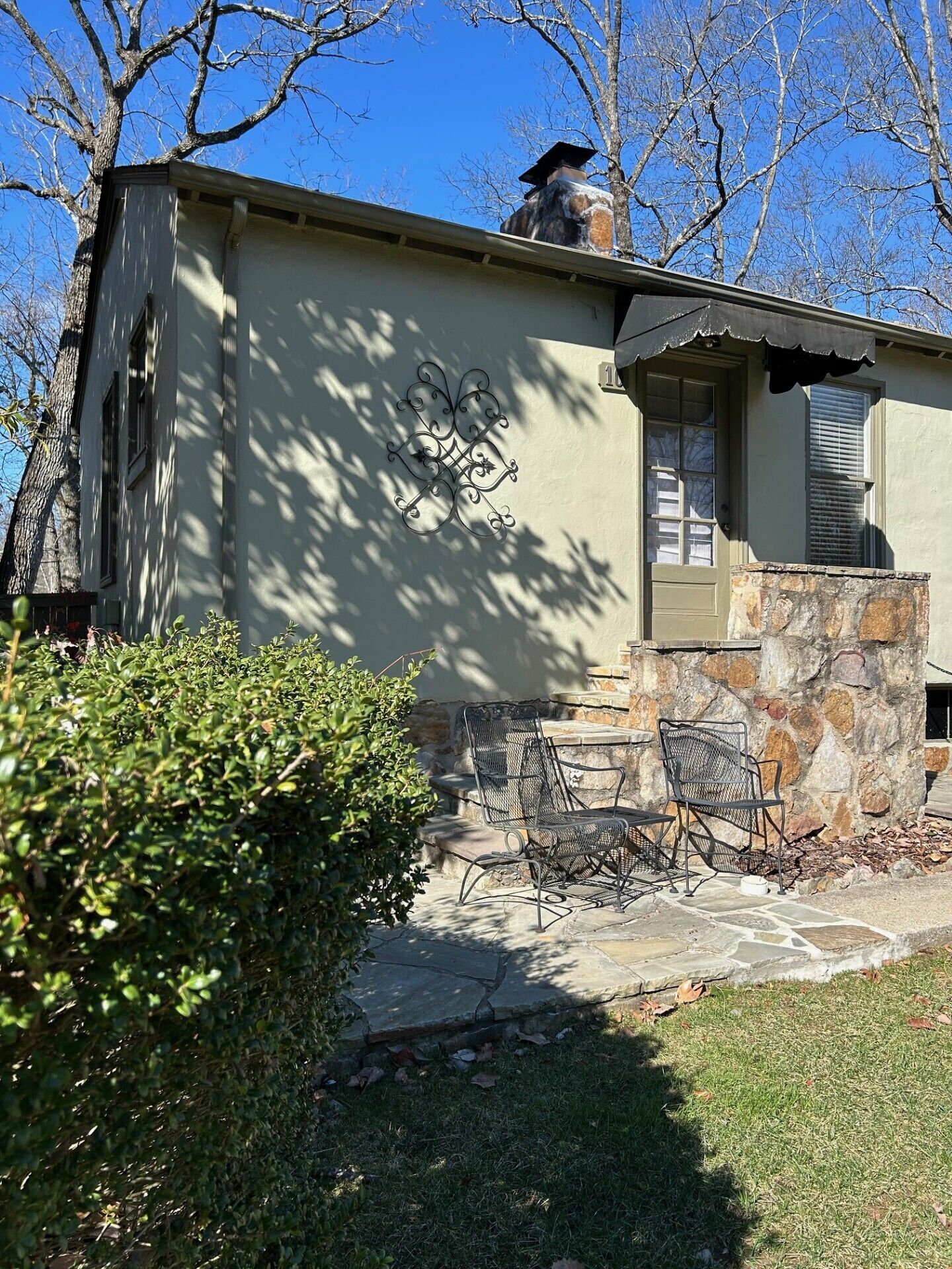 A house with a stone chimney, a metal fence, and a patio with chairs.