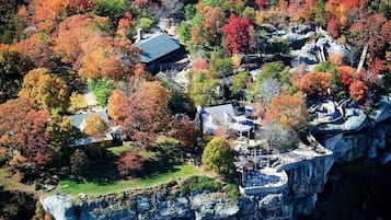 Un hôtel situé au bord d’une falaise, composé de plusieurs bâtiments, doté d’un mur de soutènement en pierre et agrémenté de divers arbres aux couleurs automnales.