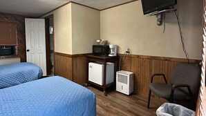 A hotel room with two beds, a desk with a computer, a TV, a microwave, a refrigerator, and a trash bin.