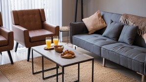 A modern living room with a grey sofa, a brown armchair, and a wooden coffee table with breakfast items.