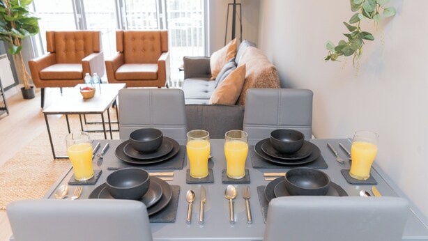 A breakfast setup with a table set for four, including plates, bowls, cutlery, and glasses of orange juice.