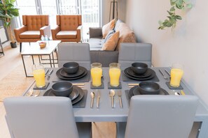 Uma mesa posta para quatro pessoas, com pratos, tigelas, talheres e copos de suco de laranja.