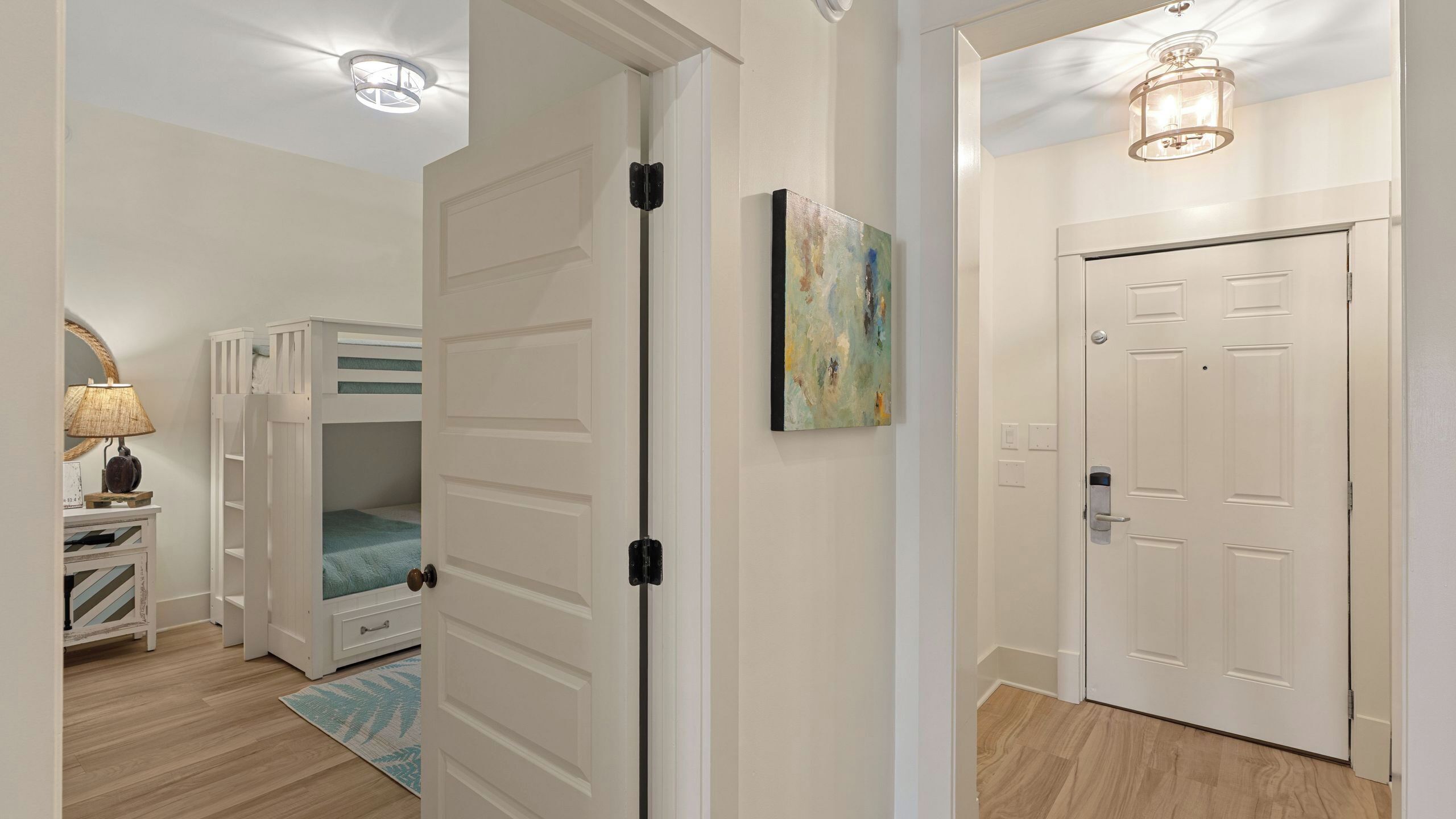 A hallway with a bunk bed, a door, a painting, and a light fixture.