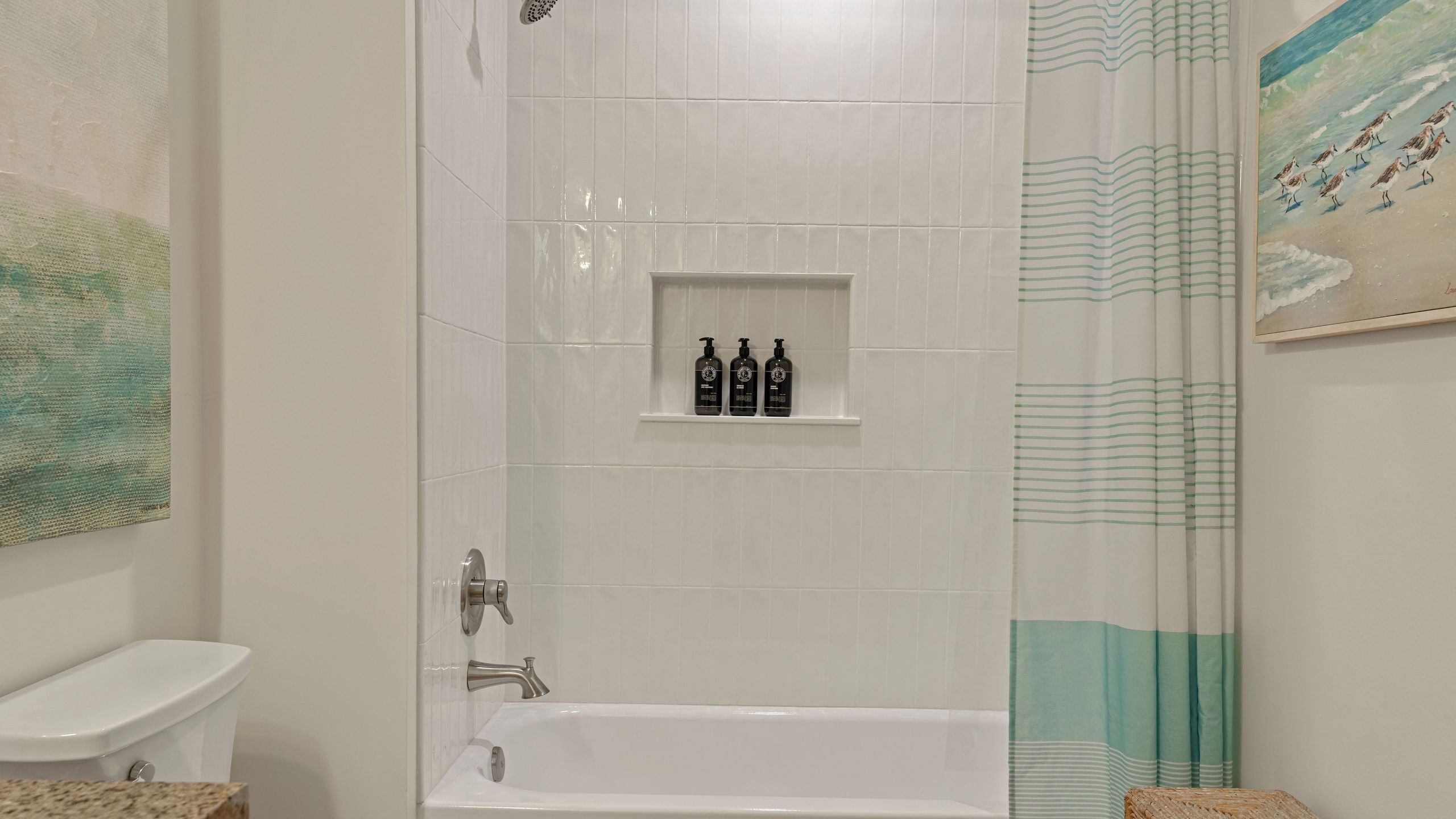 A bathroom with a bathtub, a toilet, and a shelf with three bottles.