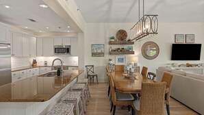 A modern kitchen with white cabinets, a stainless steel refrigerator, and a large island with stools. - 30A Kinda Day by Avantstay Pool + Private Beach Top Floor Redfish (Santa Rosa Beach)