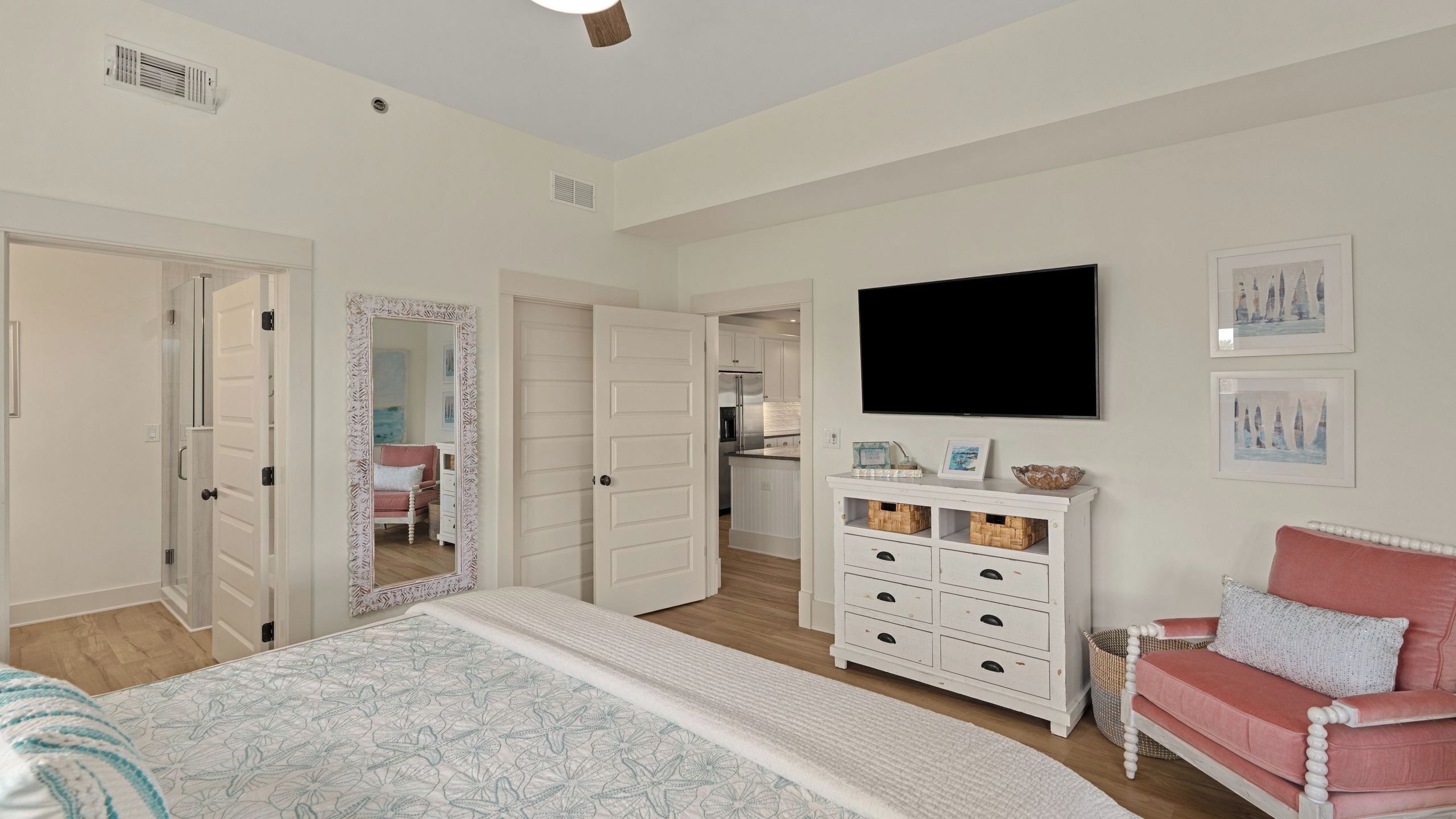 A bedroom with a bed, dresser, TV, and a hallway leading to a kitchen.