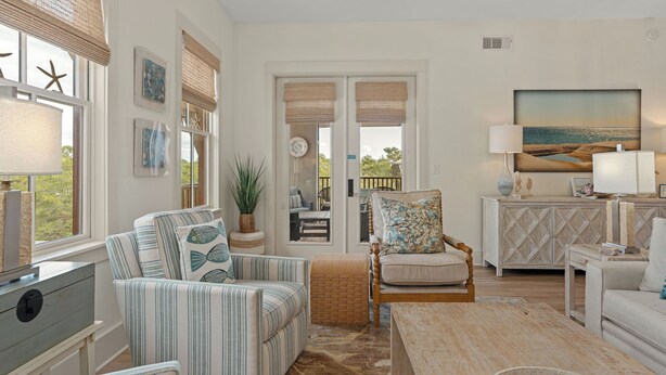 A room with a sofa, armchair, and a dining table. There is a view through a glass door to an outdoor area with a table and chairs. - 30A Kinda Day by Avantstay Pool + Private Beach Top Floor Redfish (Santa Rosa Beach)