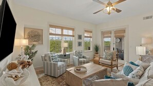 A living room with a ceiling fan, striped chairs, a coffee table, and a view of greenery outside. - 30A Kinda Day by Avantstay Pool + Private Beach Top Floor Redfish (Santa Rosa Beach)