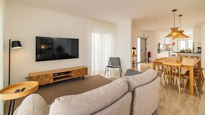 Un salon moderne doté d’un téléviseur à écran plat, d’un meuble de rangement en bois et d’un coin repas avec une table et des chaises en bois.