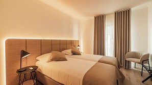 Une chambre d’hôtel avec deux lits, une petite table avec une lampe, une chaise et une vue sur l’extérieur à travers les rideaux.
