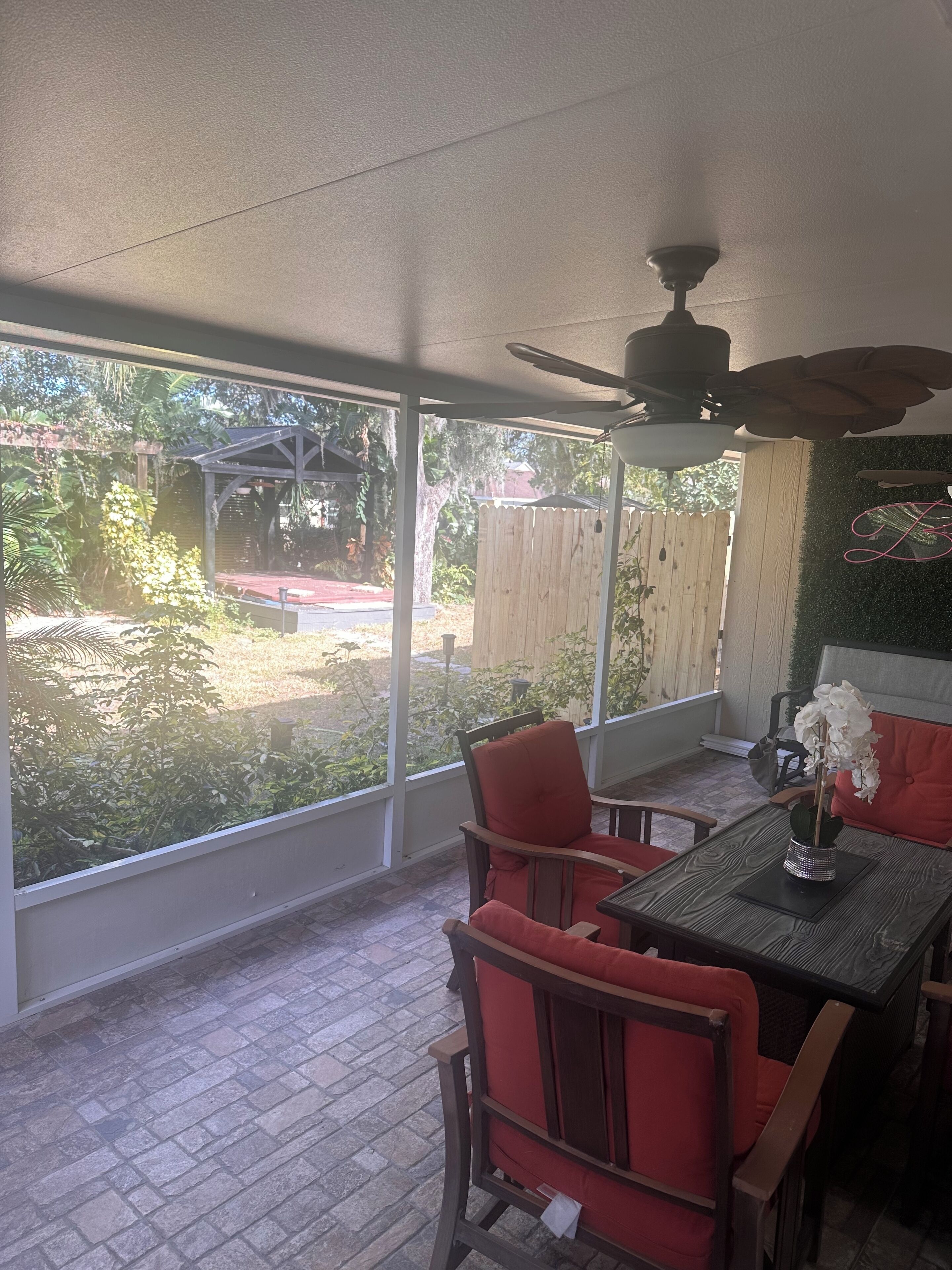 A covered patio area with a table and chairs, large windows, and a ceiling fan.