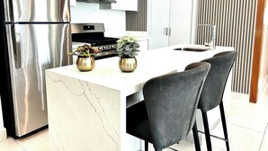Una cocina moderna con un refrigerador de acero inoxidable, una estufa y un fregadero. Hay dos jarrones dorados con plantas en la isla.
