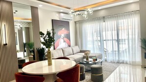 Una sala de estar moderna con una mesa de comedor redonda, sillas rojas, un sofá y un ventanal con cortinas de gasa.