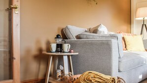 En hyggelig stue med en grå sofa, et lille træsidebord med en kaffemaskine, og en fletkurv.