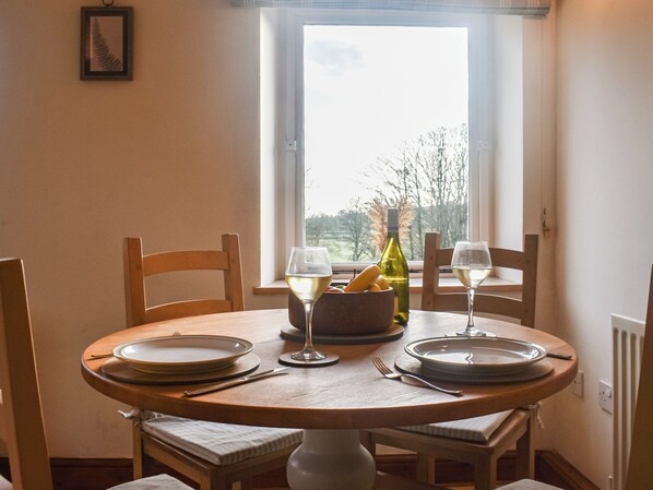 A dining table with plates, glasses, and a bottle of wine, set in a room with a window and chairs.