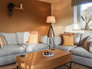 Ein modernes Wohnzimmer mit grauem Sofa, einem Holztisch und einer Stehlampe.