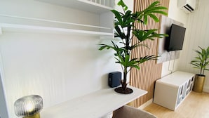 A modern living room with a white desk, a comfortable armchair, a potted plant, a flat-screen TV, and a wooden slat wall. - Studio Cocoon, sea and marina view. (Marigot)