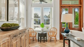 A kitchen with wooden cabinets, a dining area with wicker chairs, a ceiling fan, and a view of the outdoors through large windows.