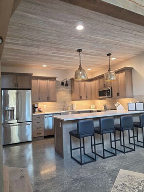 A modern kitchen with stainless steel appliances, wooden cabinets, and a central island with bar stools. - Glacier Luxury Stay • Priv Hot Tub Condo•  2BR/2BA (Coram)