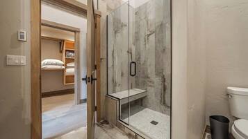 A modern bathroom with a glass-enclosed shower, a visible toilet, and a wooden door leading to a bedroom.