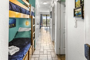 Un pasillo estrecho con literas a un lado y una puerta que da a un balcón.