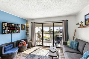 A living room with a blue wall, a Netflix sign, a sofa, a chair, and a table. - Oceanfront Condo~Heated Pool~Walk to Beach~Views (Galveston)