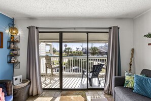 A balcony with a view of a parking lot and buildings, a grey sofa, and a wicker chair.