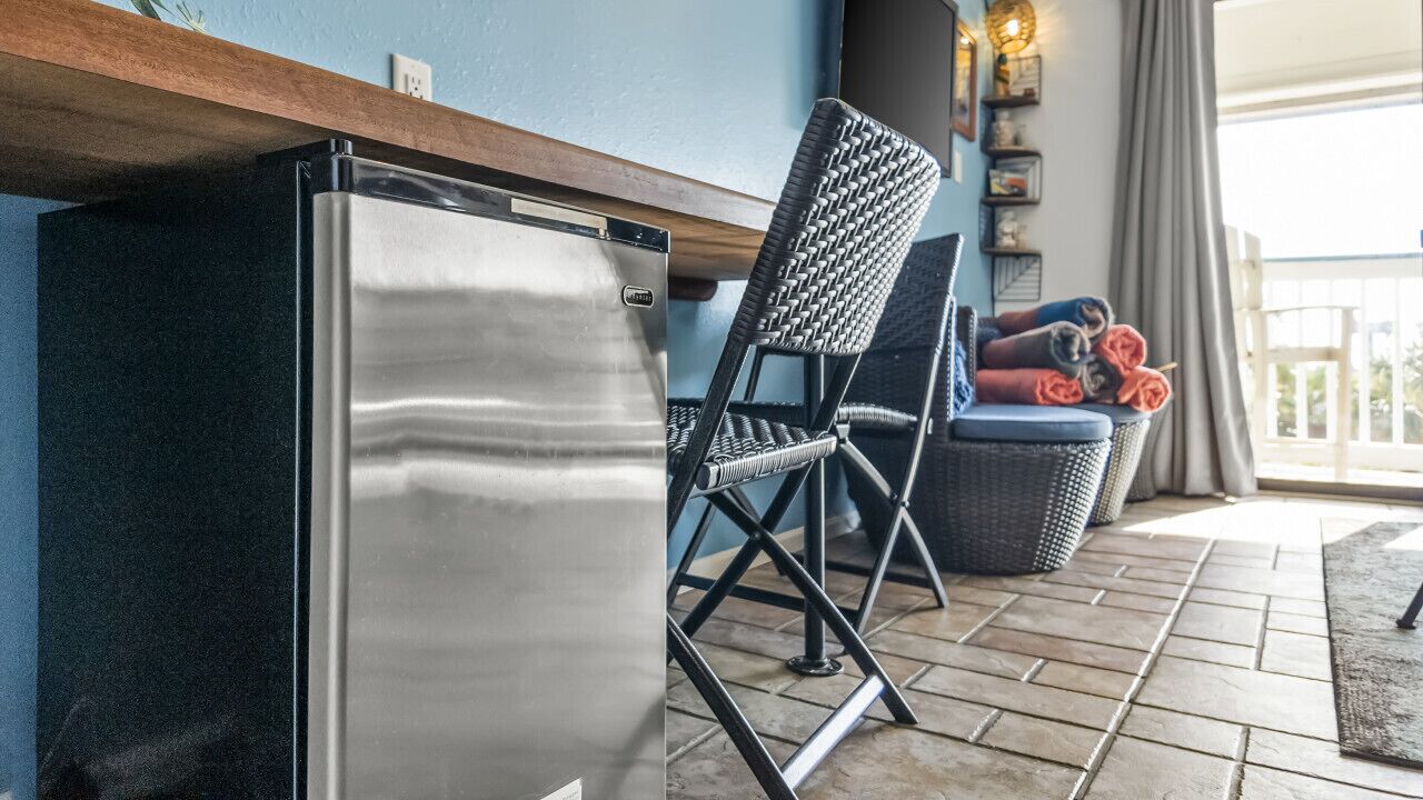 Una cocina con un refrigerador de acero inoxidable, una silla de mimbre y un sofá de mimbre con toallas enrolladas.