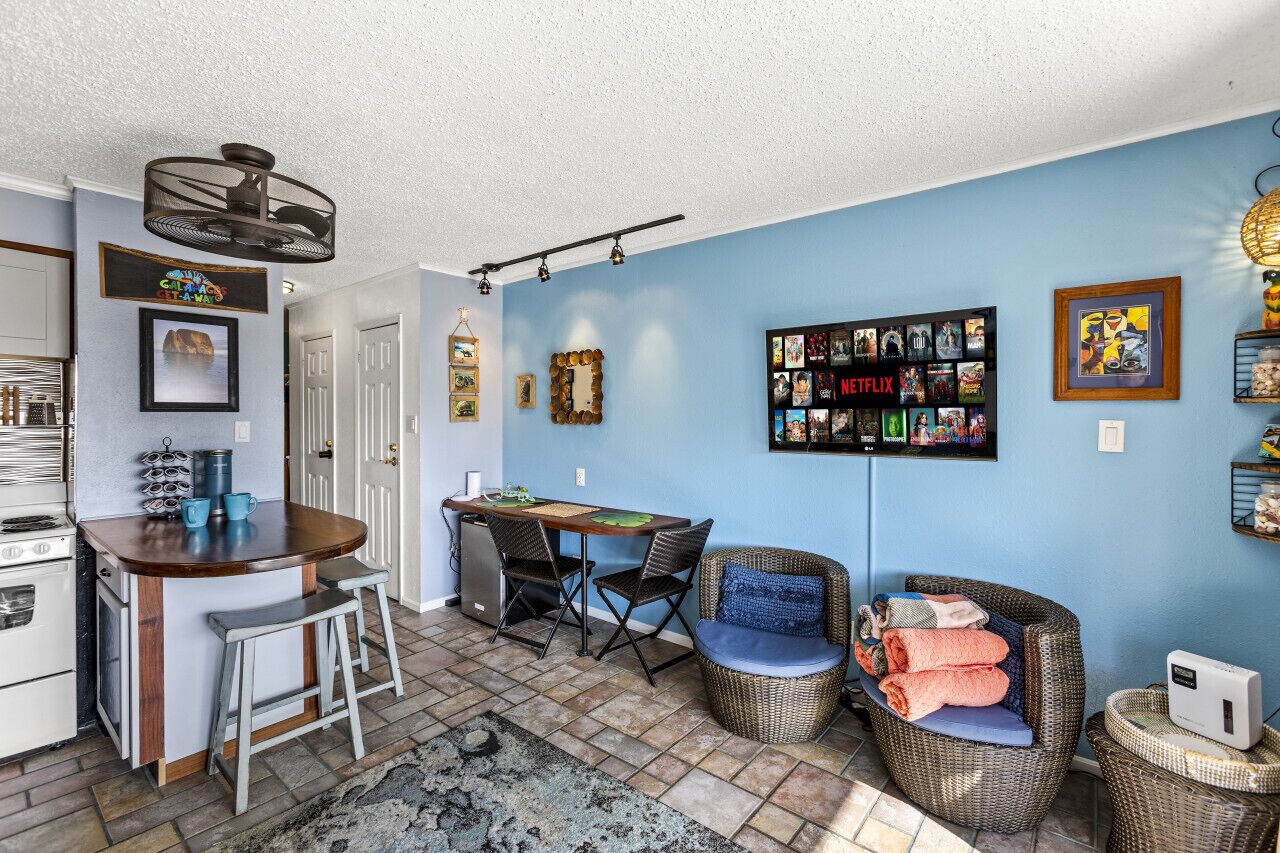 A compact kitchen with a bar area, a dining table with chairs, and a seating area with a wicker chair and a small table.