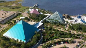 Vista aérea de un resort con un gran edificio en forma de pirámide, un invernadero de vidrio y una masa de agua.