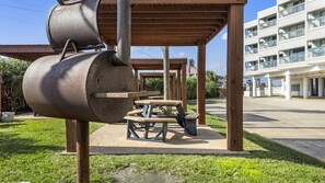 Un espacio al aire libre techado con una parrilla para barbacoa, mesas de picnic y un edificio al fondo.