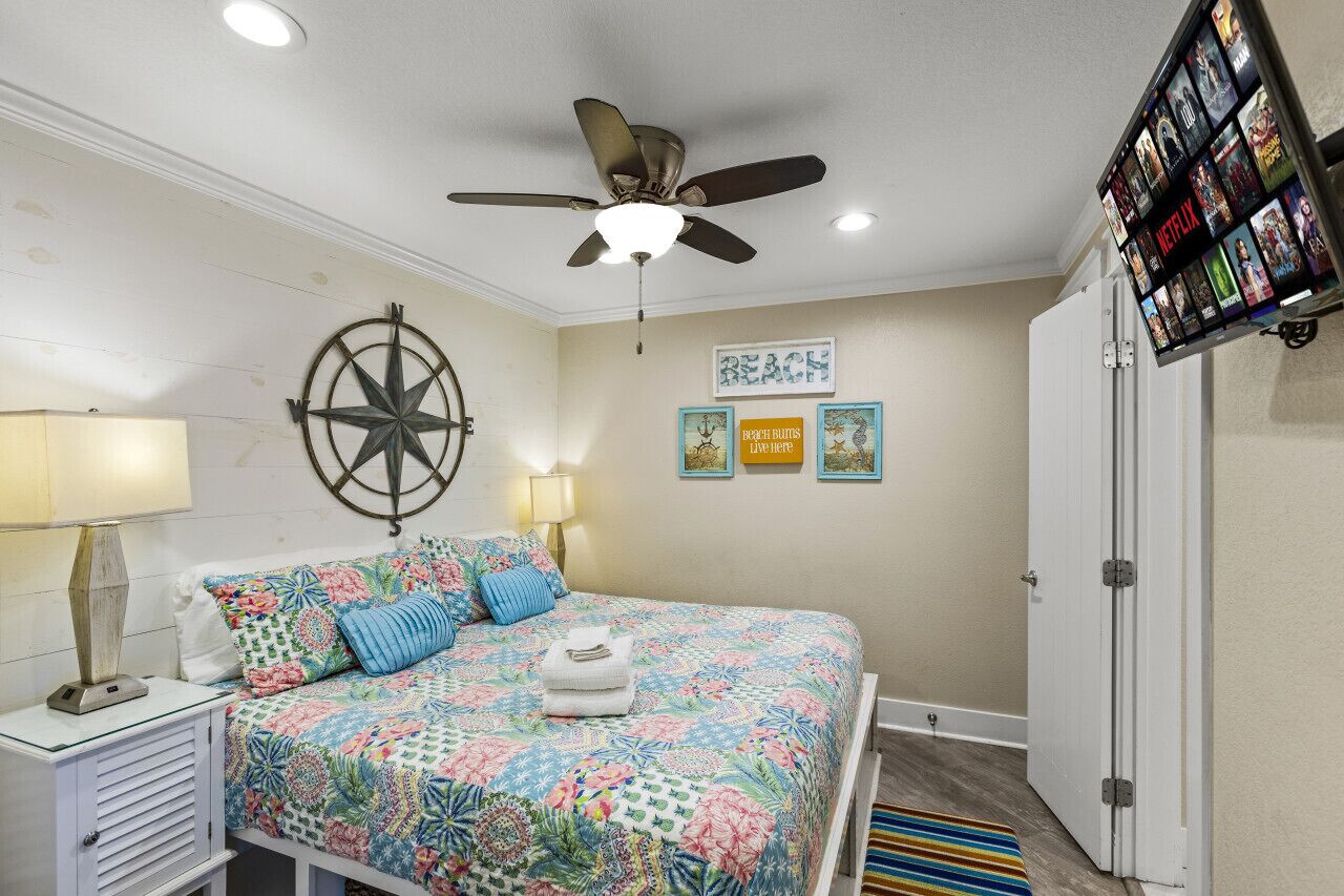A bedroom with a bed, a ceiling fan, a wall-mounted TV, and a door.