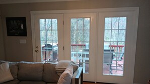 A living room with a sectional sofa, a coffee table, and a rug. There are three large windows with a view of a deck and outdoor furniture. - Large Beautiful quality home in a quiet subdivision.  (Lynchburg)