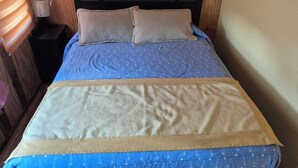 A bed with a blue and beige bedspread, a wooden headboard, and a nightstand with a lamp. - Cabaña Galvarino Puerto Natales (Natales)